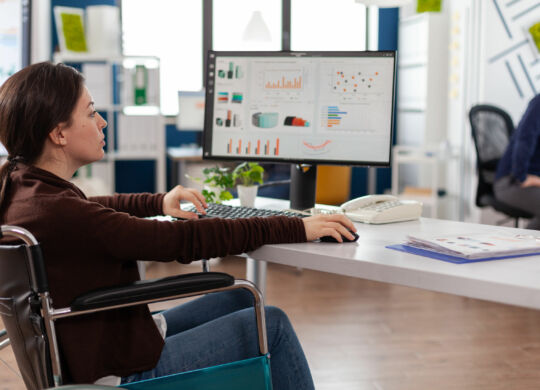 Paralyzed businesswoman in wheelchair typing marketing strategy working at company presentation in startup business office. Disabled manager analyzing management digital report on computer