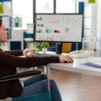 Paralyzed businesswoman in wheelchair typing marketing strategy working at company presentation in startup business office. Disabled manager analyzing management digital report on computer
